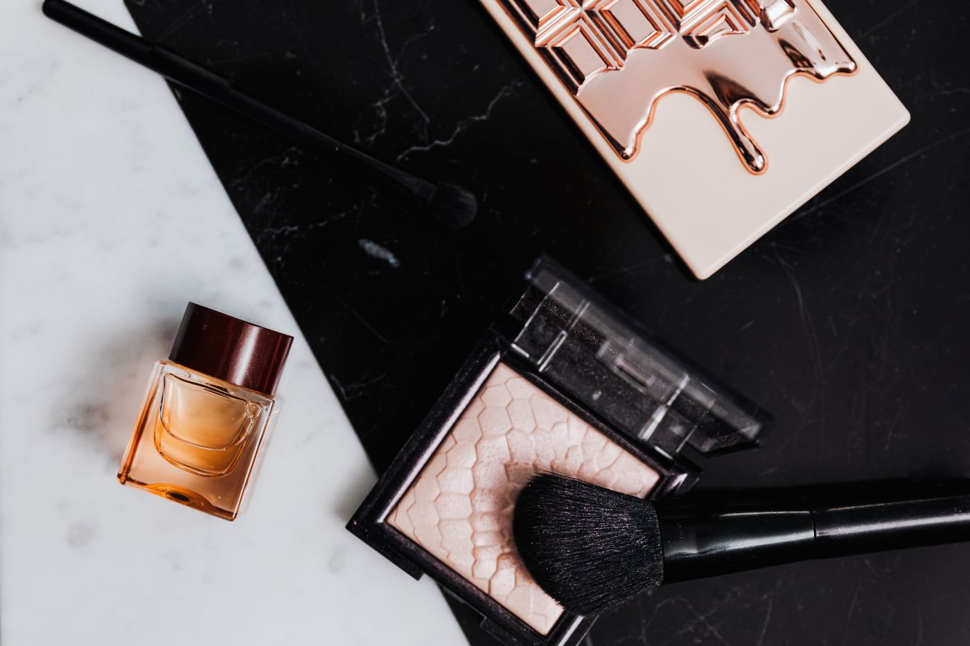 A high-angle view of beauty products including eyeshadow, lipstick and perfume on marble and black backgrounds